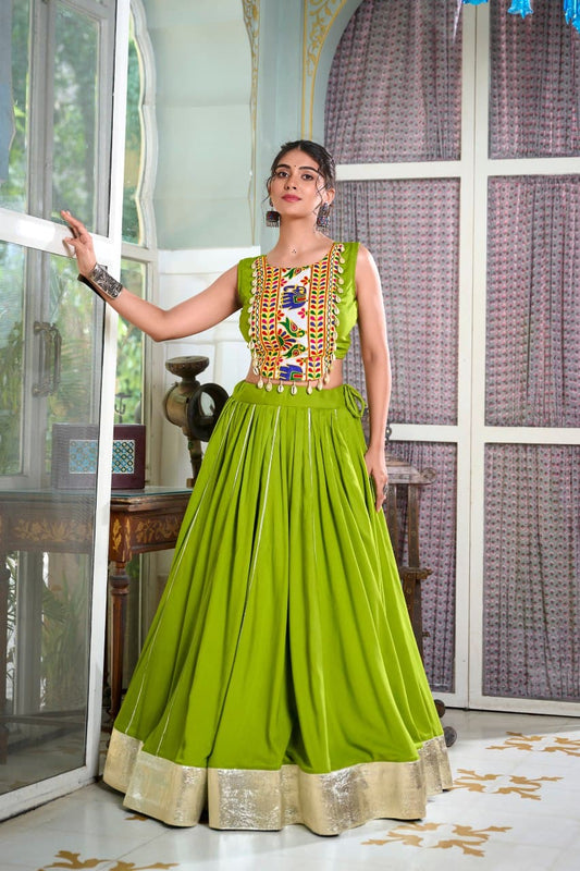 Woman in a green traditional outfit with intricate patterns standing indoors.